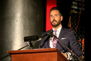 A Man in a Grey Coat Speaking on the Stage